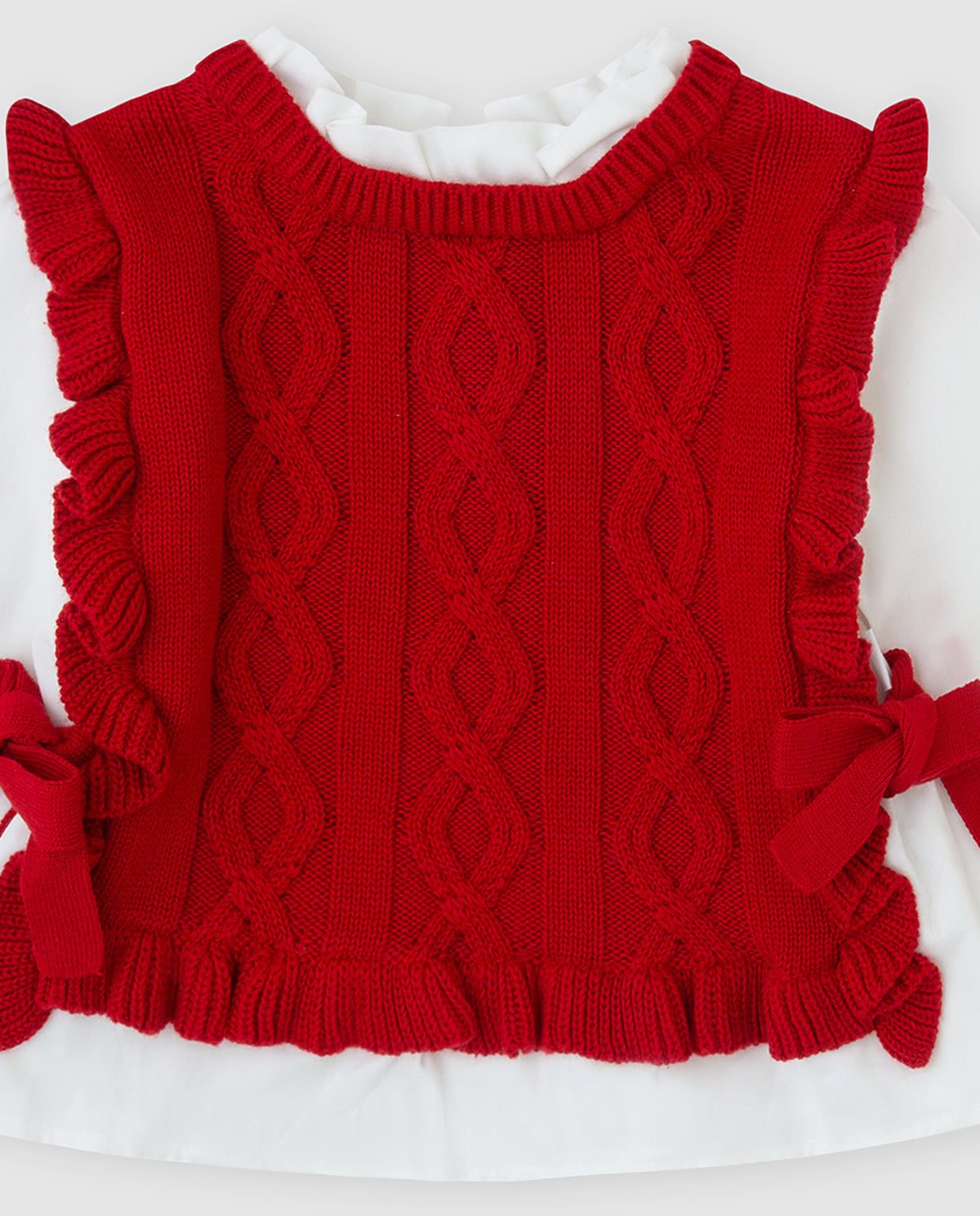 Detailfoto Tutto Piccolo rode gebreide meisjestrui - kabelknitpatroon met diamantvorm en ruffle rand aan de zijkant met rood strikje