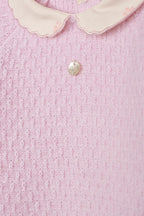 Detailopname roze gebreide stof, peterkraagje en parelmoer knopje babypakje DK101