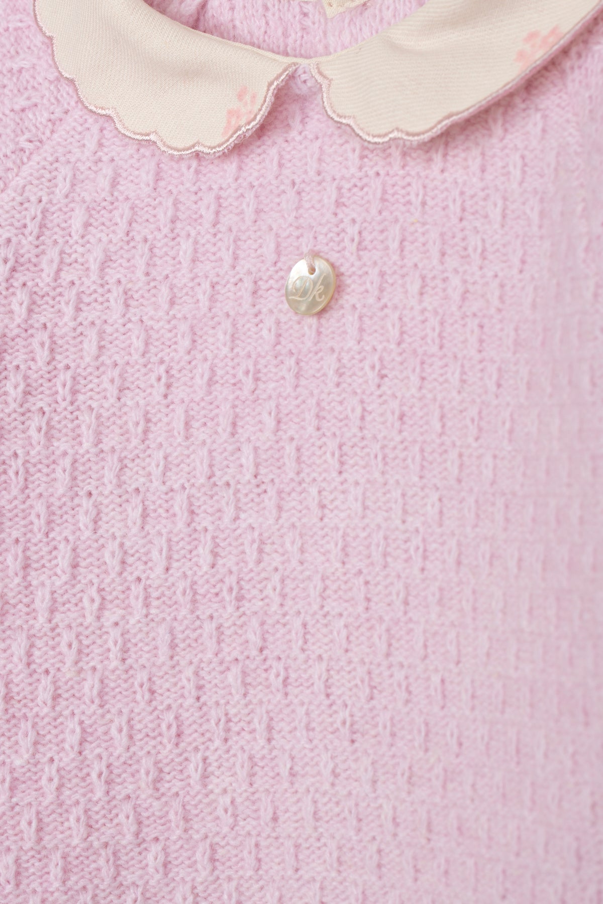 Detailopname roze gebreide stof, peterkraagje en parelmoer knopje babypakje DK101
