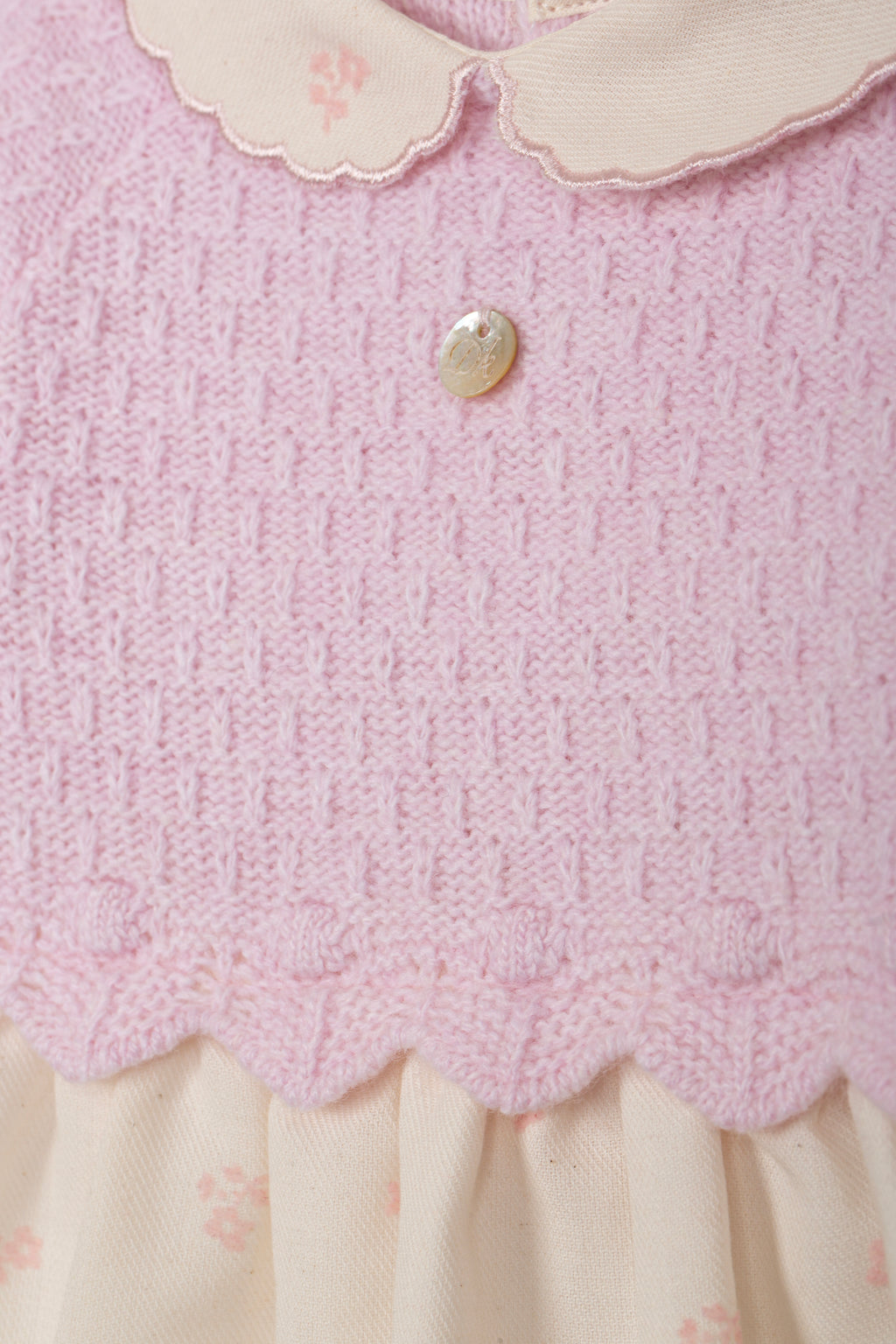 Detailopname roze gebreide stof, scallop-rand en parelmoer knopje babyjurk DK108