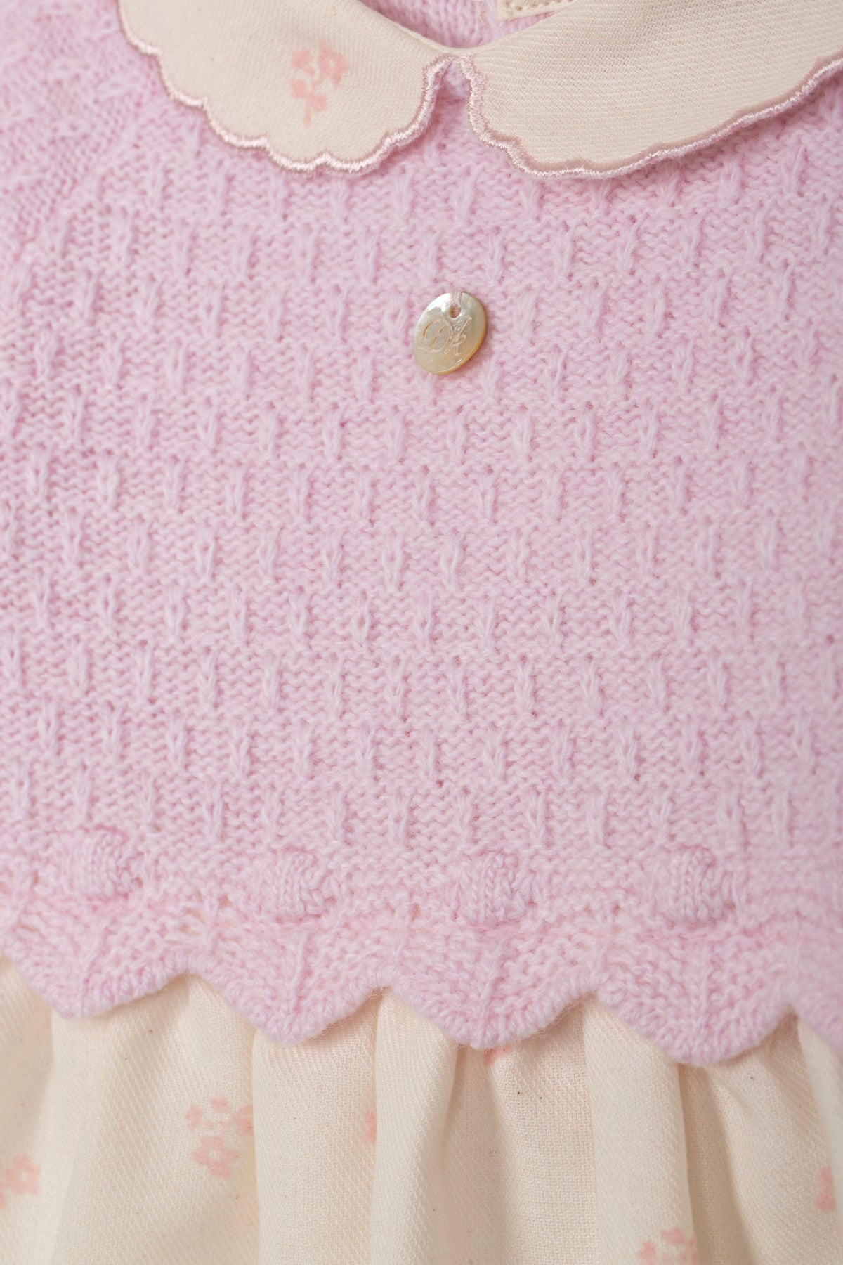 Detailopname roze gebreide stof, scallop-rand en parelmoer knopje babyjurk DK108