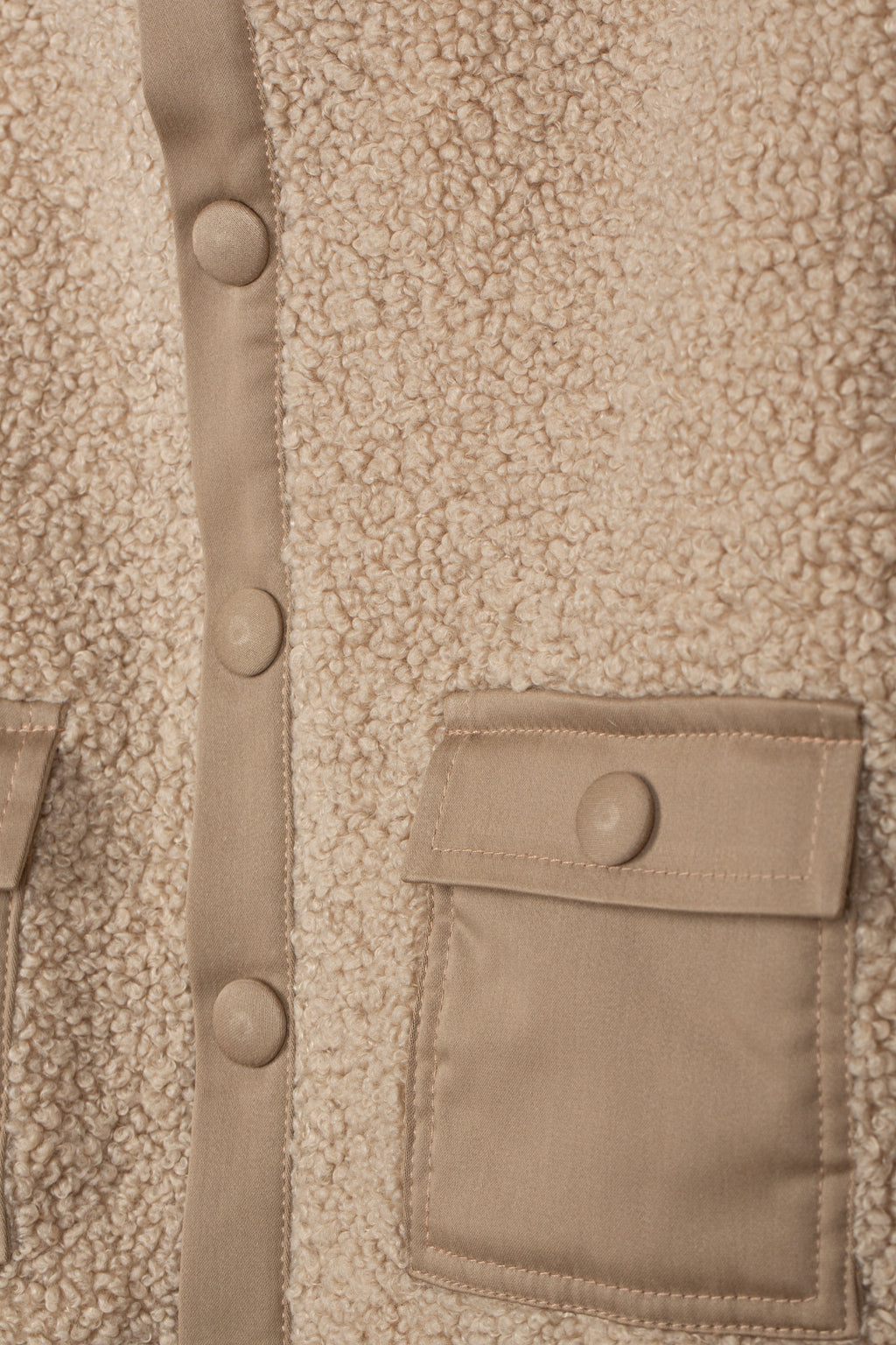 Detail van de teddystructuur, drukknoopsluiting en zak met klep van de beige jas
