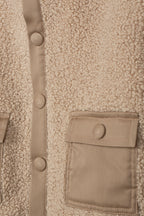 Detail van de teddystructuur, drukknoopsluiting en zak met klep van de beige jas