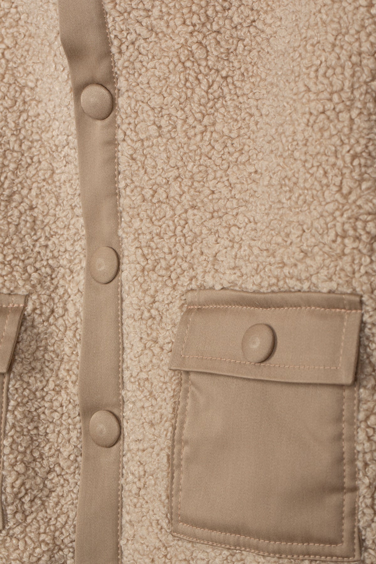 Detail van de teddystructuur, drukknoopsluiting en zak met klep van de beige jas