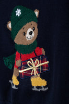 Detail van de beer met groene muts, sjaal, schaatsen en cadeau op de donkerblauwe trui