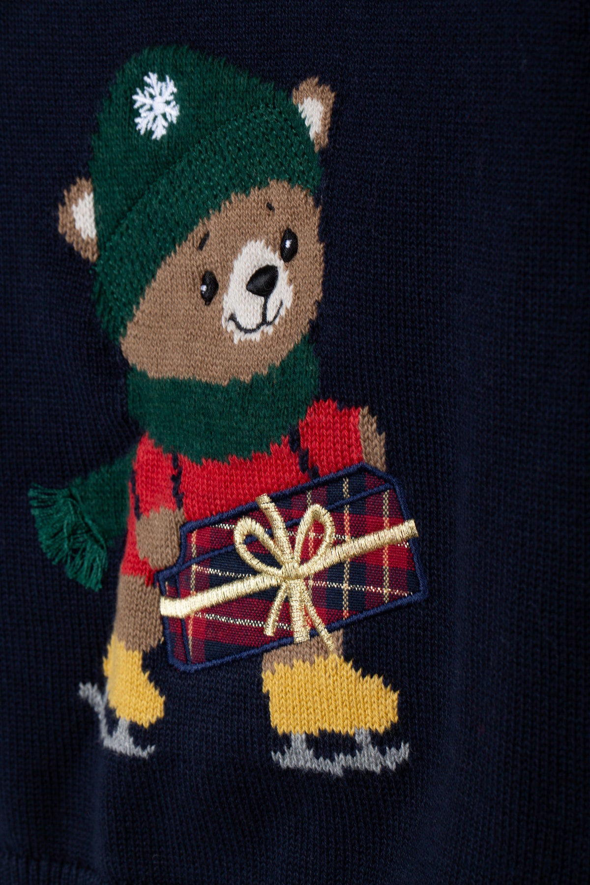 Detail van de beer met groene muts, sjaal, schaatsen en cadeau op de donkerblauwe trui