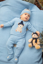 Baby in lichtblauw gebreid babypakje met teddybeer motief en bijpassend mutsje – sfeerbeeld