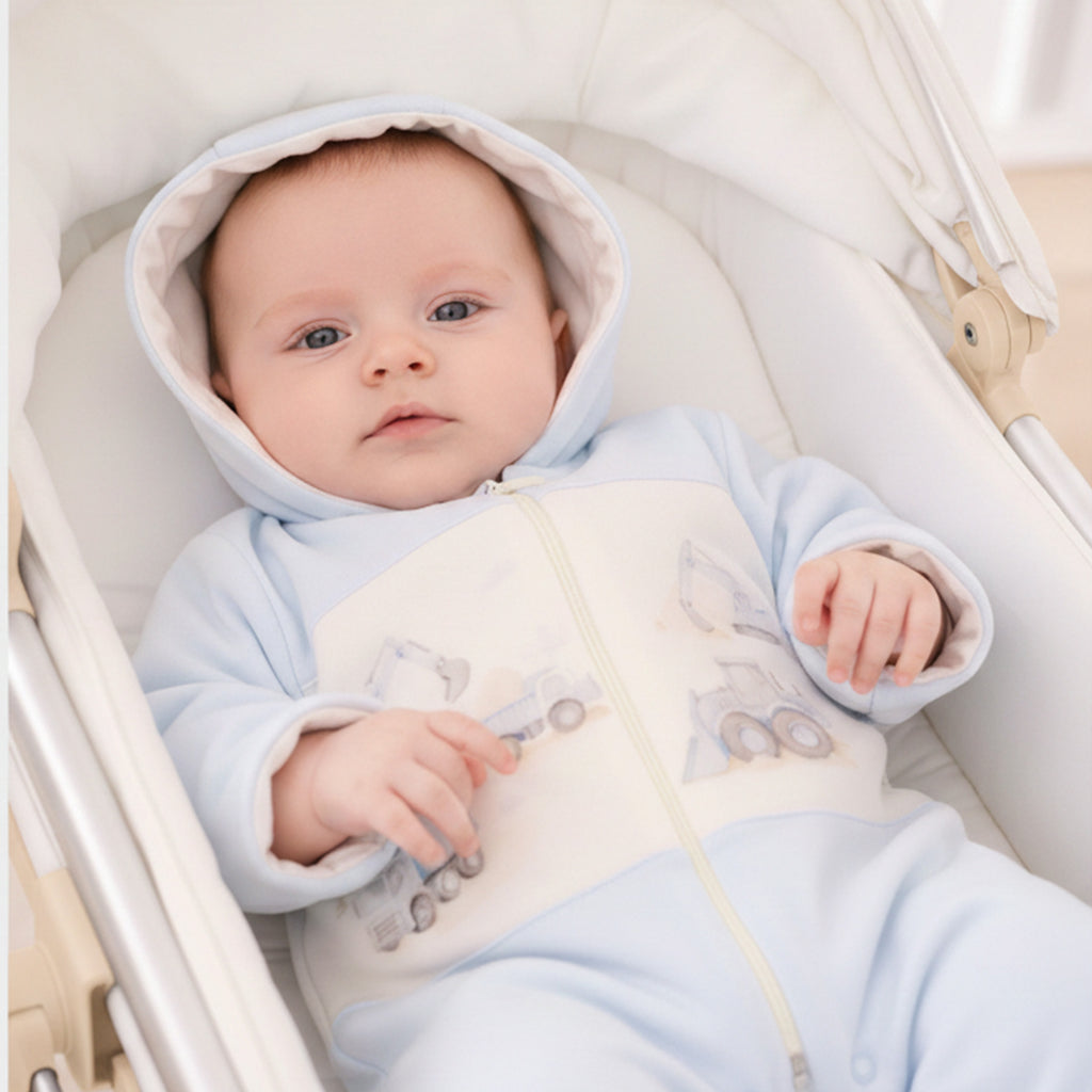 Baby jongen in lichtblauw beerpakje met capuchon en voertuig print, liggend in een witte wieg – MATTY Sofija