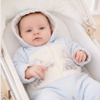 Baby jongen in lichtblauw beerpakje met capuchon en voertuig print, liggend in een witte wieg – MATTY Sofija
