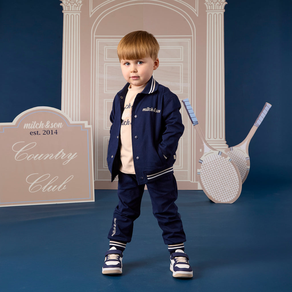 Jongen in 2-delige navy blauwe bomberjack set van Mitch & Son met witte streepdetails, Country Club collectie