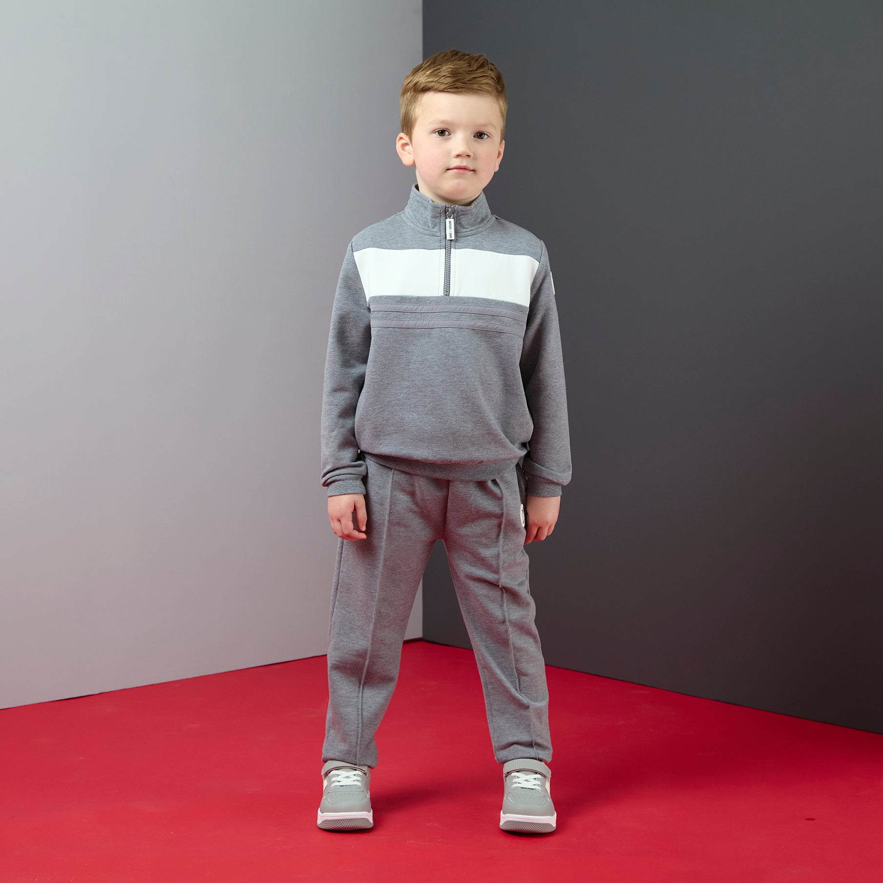 Jongen in grijze 2-delige joggingset van Mitch & Son met half-zip sweater en wit kleurblok, gedragen met sneakers

