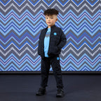 Jongen in navy Mitch & Son Winston & Waleed pak met gewatteerde bomberjack en lichtblauwe badge, gecombineerd met lichtblauw shirt en sneakers


